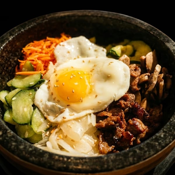Bibimbap in a stone bowl with fried egg, beef, carrots, cucumbers, and mushrooms.