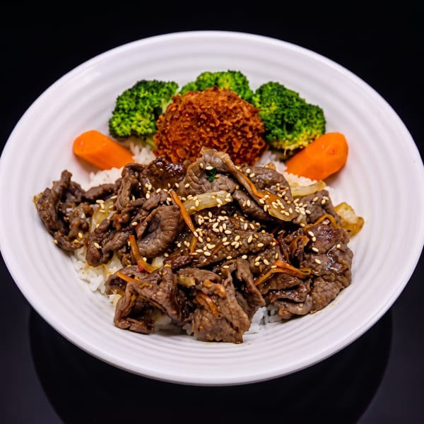 A white bowl filled with rice, beef, broccoli, carrots, and a fried croquette.