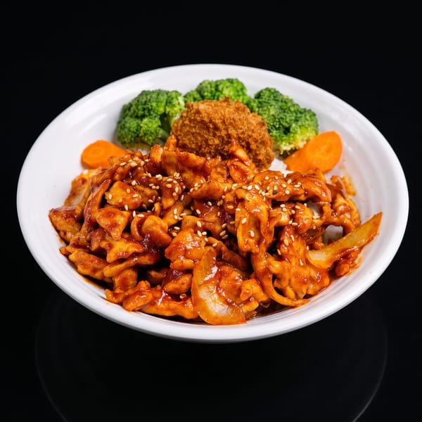 Spicy chicken with sesame seeds, broccoli, carrots, and a fried croquette in a white bowl.