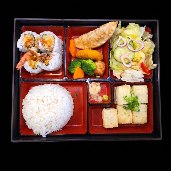 A bento box filled with sushi rolls, fried dumplings, salad, rice, and fried tofu.