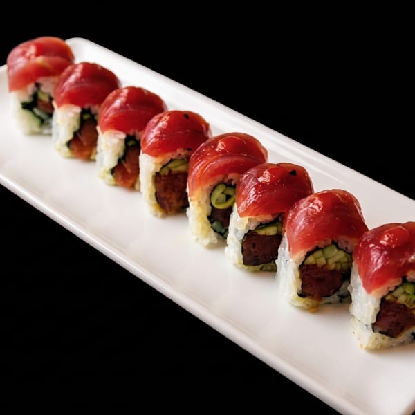 Eight pieces of tuna sushi rolls with cucumber and rice, served on a white rectangular plate.