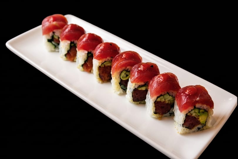 Eight pieces of tuna sushi rolls with cucumber and rice, served on a white rectangular plate.
