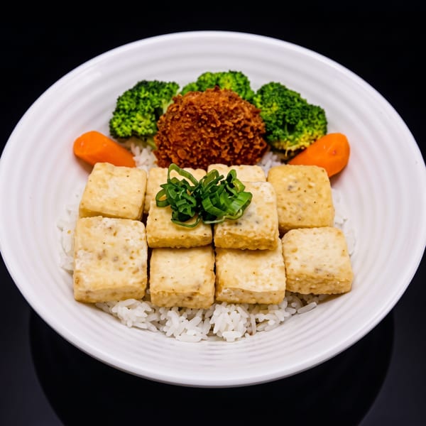A white bowl filled with rice, fried tofu, broccoli, carrots, and a crispy brown croquette.