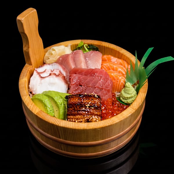 Chirashi sushi in a wooden bowl with tuna, salmon, octopus, eel, avocado, roe, and wasabi.