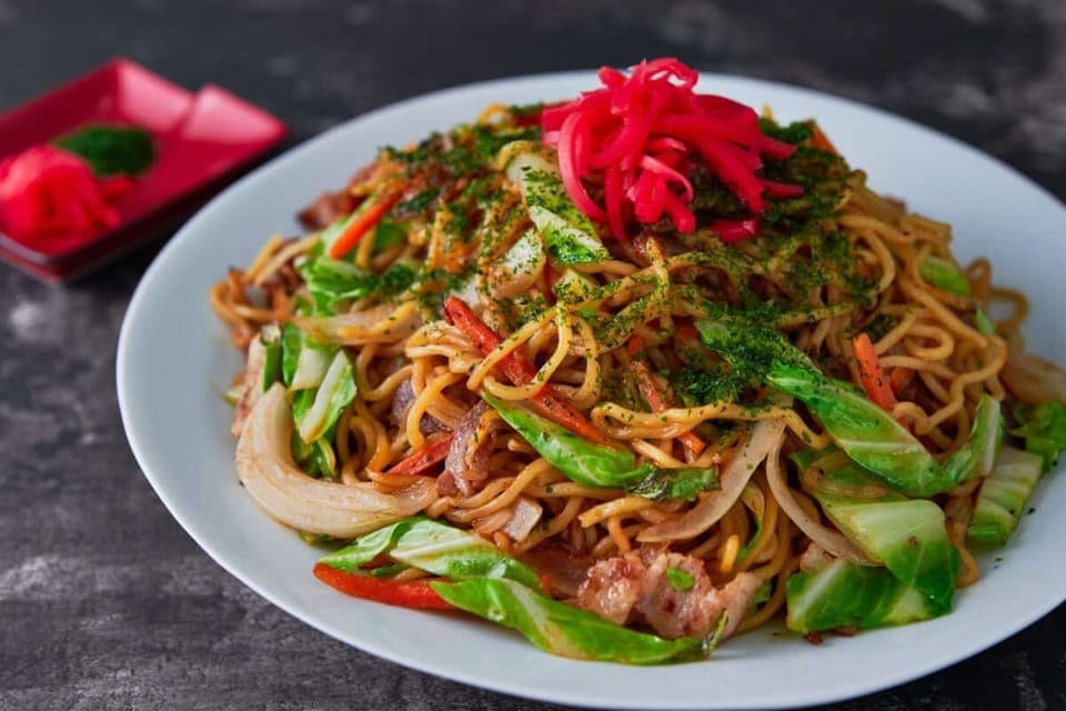A plate of yakisoba noodles with cabbage, carrots, meat, and red pickled ginger.