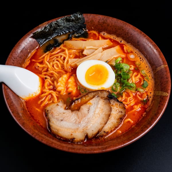 Spicy ramen bowl with pork belly, soft-boiled egg, bamboo shoots, green onions, and nori.
