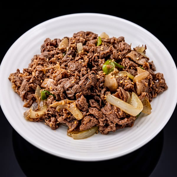 Bulgogi, Korean BBQ beef, with sesame seeds, onions, and green peppers on a white plate.